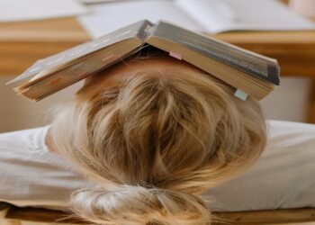 Ragazza delle scuole superiori con dei libri sulla testa.