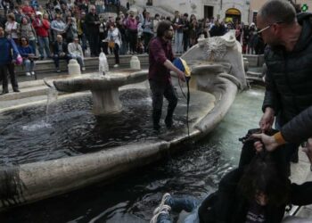 Attivisti di Ultima Generazione mentre sporcano con vernice nera la fontana della  Barcaccia in Piazza di Spagna a Roma (LaPresse)