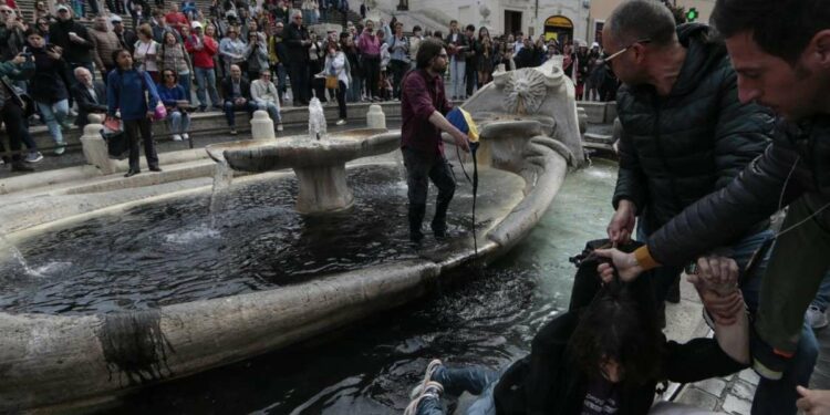 Attivisti di Ultima Generazione mentre sporcano con vernice nera la fontana della  Barcaccia in Piazza di Spagna a Roma (LaPresse)